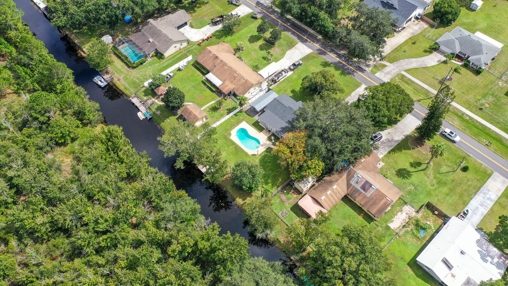 drone shot of top of homes with brown and grey roofs and open canal with trees
